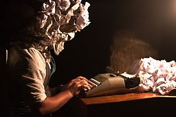 A writer whose head is composed of crumpled paper uses a typewriter.