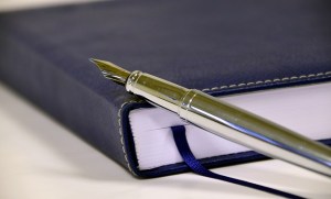 Gold fountain pen leaning on a closed black leather-bound book